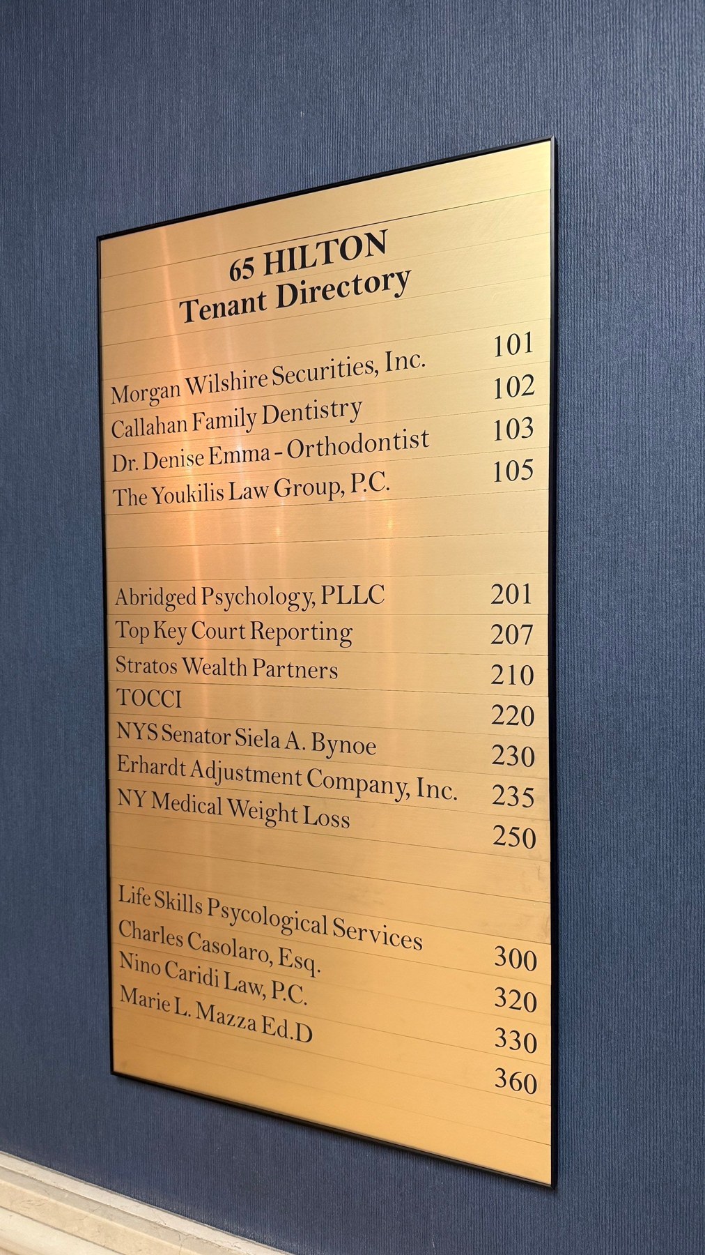 Gold-toned tenant directory mounted on a dark wall